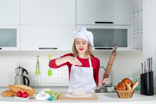 正面図キッチンのまな板の上に生地に小麦粉を振りかける若い女性料理人