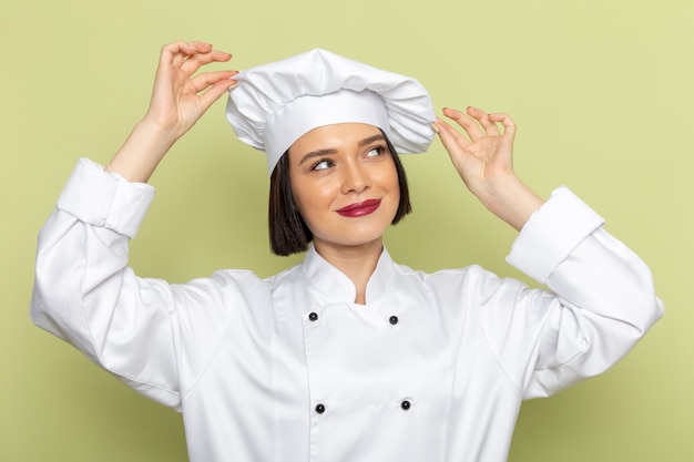 흰색 요리사 양복과 모자 포즈와 녹색 벽에 꿈을 꾸고 전면보기 젊은 여성 요리사 레이디 작업 음식 요리 색상