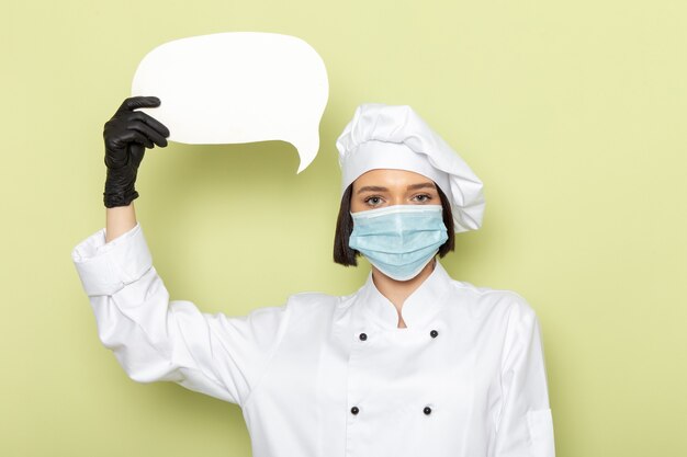 A front view young female cook in white cook suit and cap wearing gloves and sterile mask on the green wall lady work food cuisine color