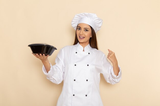 Front view of young female cook in white cook suit holding bowl on white wall