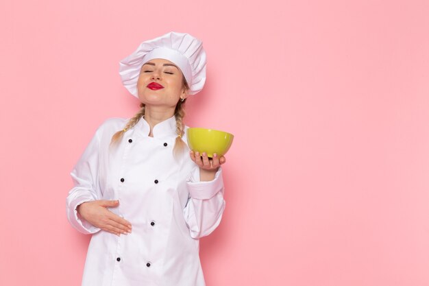 ピンクのスペースクックにグリーンプレートを保持している白いクックスーツで正面の若い女性クック