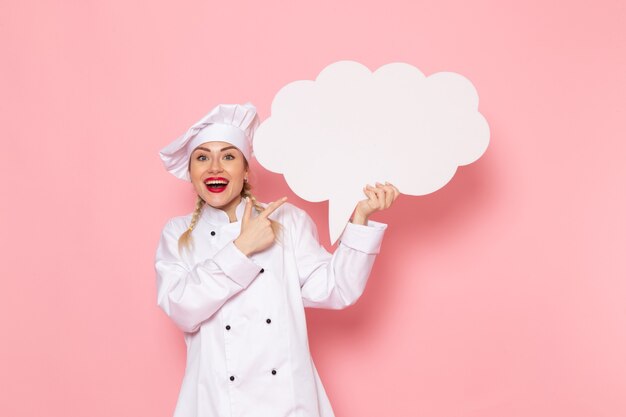 핑크 공간 요리사에 기쁘게 표정으로 흰색 기호를 들고 흰색 요리사 정장에 전면보기 젊은 여성 요리사 photo