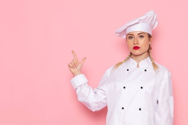 Free photo front view young female cook in white cook suit just posing and standing on the pink space