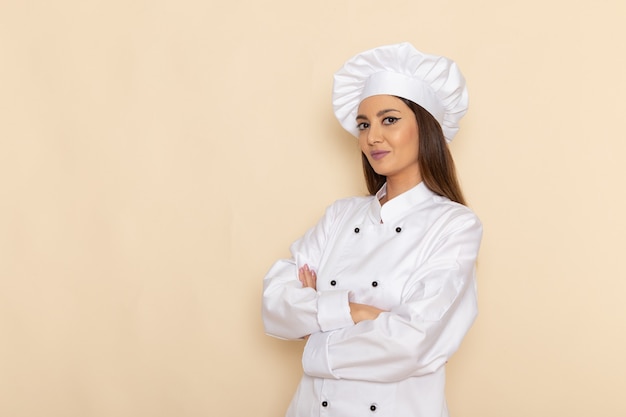 Free photo front view of young female cook in white cook suit posing with smile on light-white wall