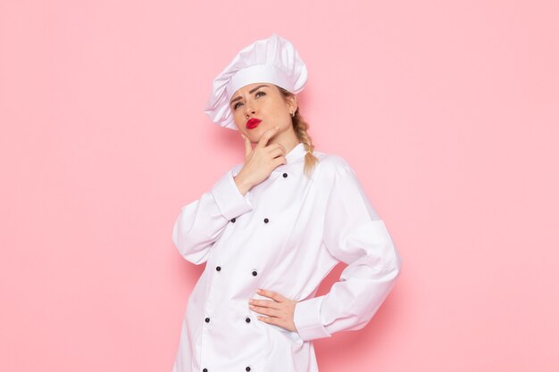 Front view young female cook in white cook suit posing with thinking expression on the pink space cook cuisine job work  photo