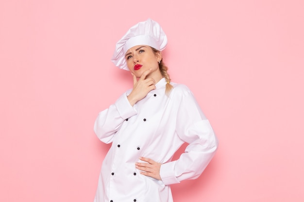 Вид спереди молодая женщина-повар в белом костюме повара позирует с выражением мышления на розовом пространстве, повар кухня работа работа фото