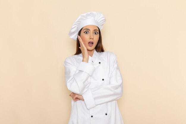 Front view of young female cook in white cook suit showing surprissed expression on light-white wall