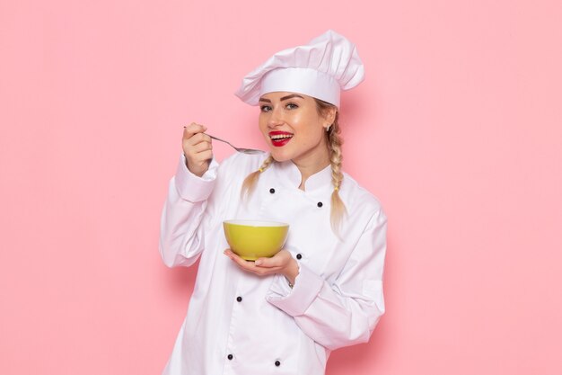 Front view young female cook in white cook suit tasting soup with smile on the pink space cook cuisine job work  photo