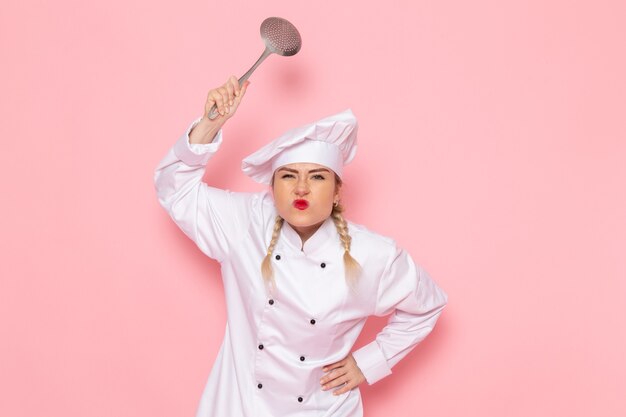 Front view young female cook in white cook suit threatening with silver spoon on the pink space cook cuisine job work  photo