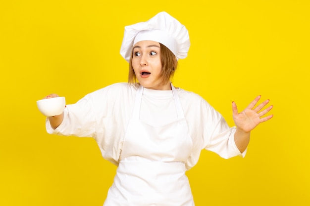 흰색 쿡 양복과 흰색 컵을 들고 흰색 모자에 전면보기 젊은 여성 요리사는 노란색에 재미 흥분