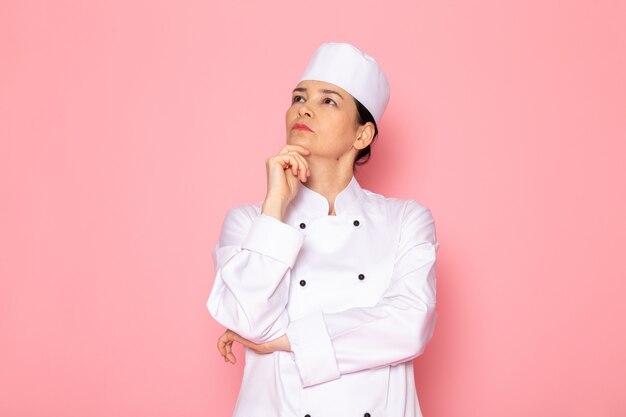 Вид спереди молодая женщина-повар в белом костюме повара белая шапочка позирует выражение глубокого мышления