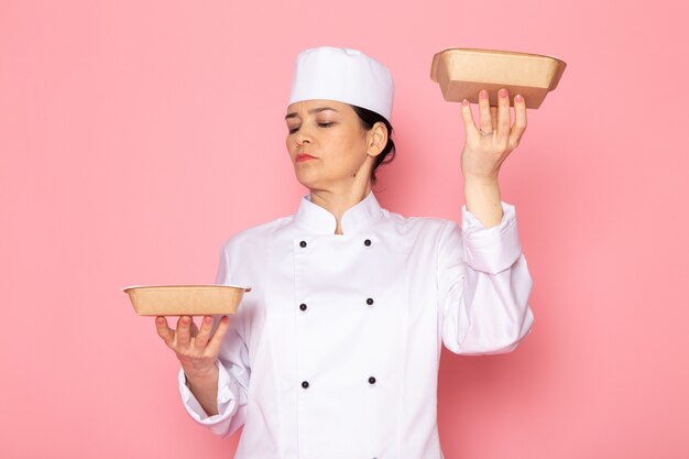 우유 갈색 그릇을 들고 포즈 흰색 쿡 정장 흰색 모자에 전면보기 젊은 여성 요리사