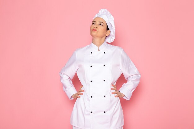 A front view young female cook in white cook suit white cap posing looking into the above distance