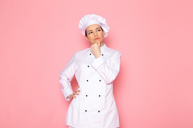 A front view young female cook in white cook suit white cap posing thinking deeply