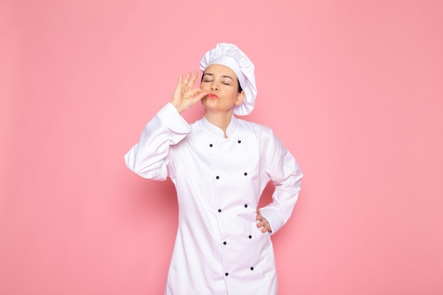 Un giovane cuoco femminile di vista frontale in berretto bianco vestito bianco del cuoco che sorride posando segno delizioso felice