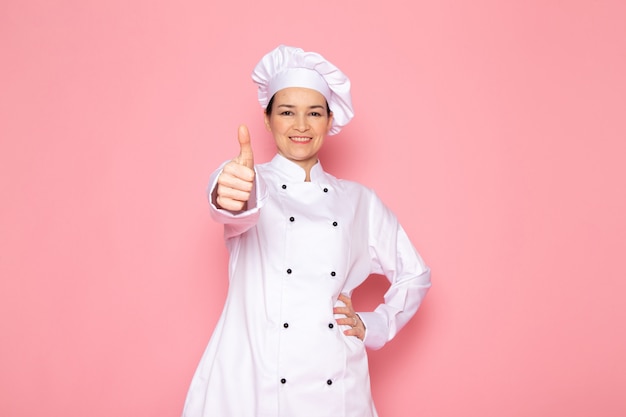 A front view young female cook in white cook suit white cap smiling posing happy