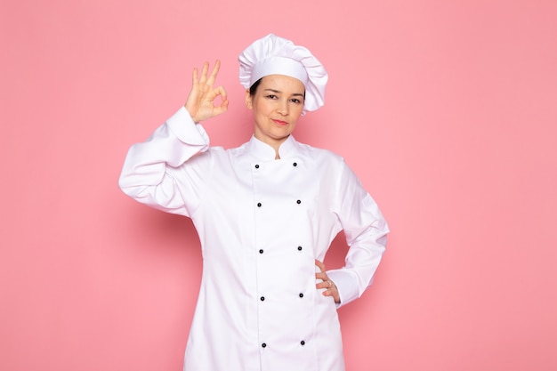 A front view young female cook in white cook suit white cap smiling posing