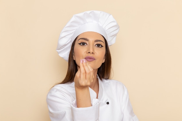 Front view of young female cook in white cook suit on white wall