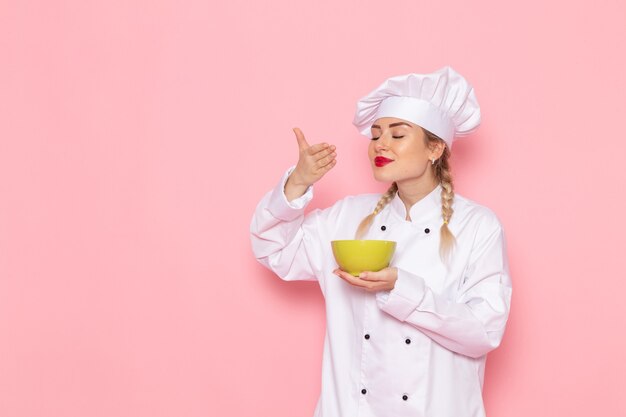 Front view young female cook in white suit smelling food on the pink space cook cuisine job work  photo