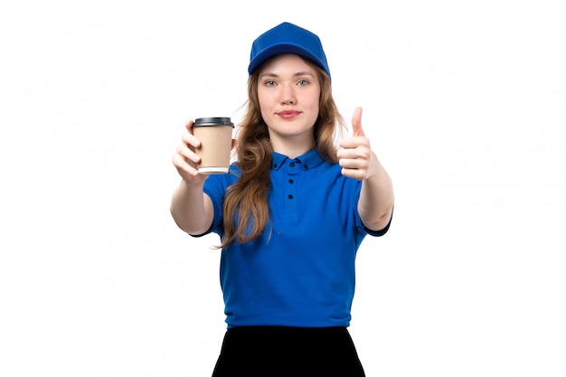 A front view young female courier in blue shirt blue cap and black trousers holding cup of coffee on white