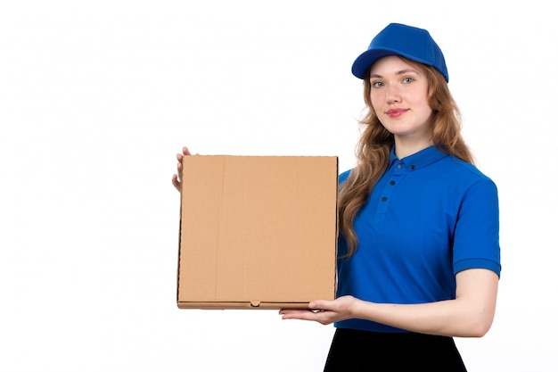 Un giovane corriere femminile di vista frontale in cappuccio blu della camicia blu e pantaloni neri che tengono la scatola di consegna che sorride sul bianco
