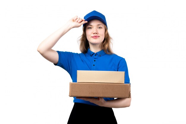 A front view young female courier in blue shirt blue cap and black trousers holding delivery boxes smiling on white