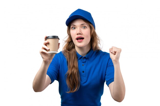 A front view young female courier in blue shirt blue cap holding cup of coffee cheering on white