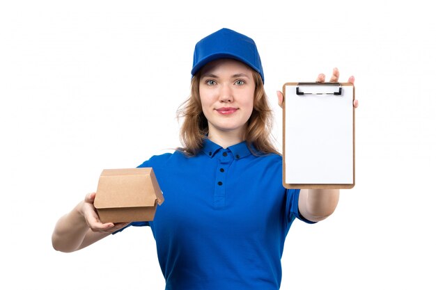 A front view young female courier in blue shirt blue cap smiling holding food package and notepad on white