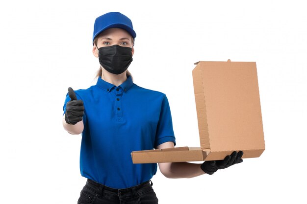 A front view young female courier in blue uniform black gloves and black mask holding food delivery package