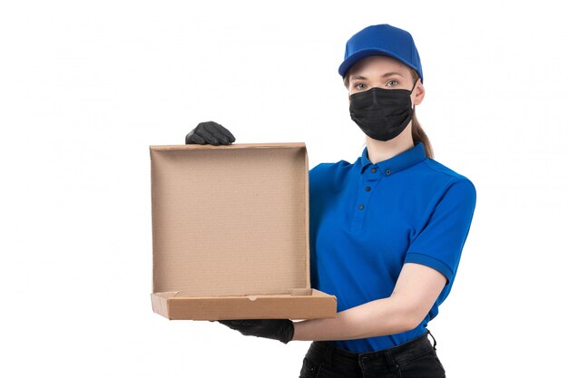 Молодая женщина-курьер в синей форме, черных перчатках и черной маске, держащая пакет для доставки еды, вид спереди
