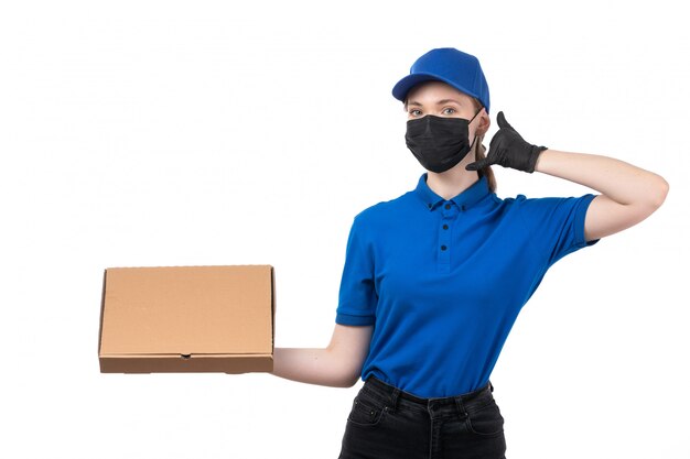 A front view young female courier in blue uniform black gloves and black mask holding food delivery package