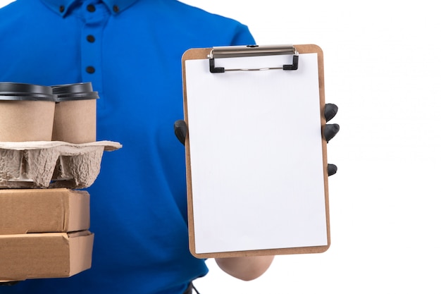 Foto gratuita un giovane corriere femminile di vista frontale in guanti neri uniformi blu e maschera nera che tiene i pacchetti e il blocco note di consegna dell'alimento