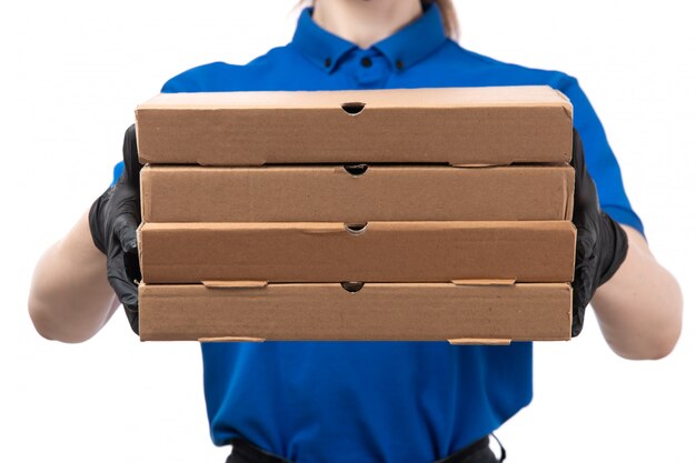 A front view young female courier in blue uniform black gloves and black mask holding food delivery packages