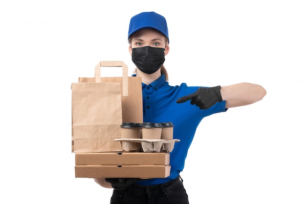 Un giovane corriere femminile di vista frontale in guanti neri uniformi blu e maschera nera che tiene i pacchetti di consegna dell'alimento