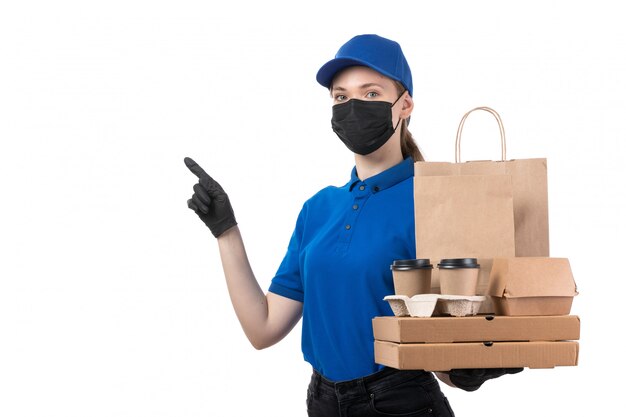 Молодая женщина-курьер в синей форме, черных перчатках и черной маске, держащая посылки с доставкой еды, вид спереди