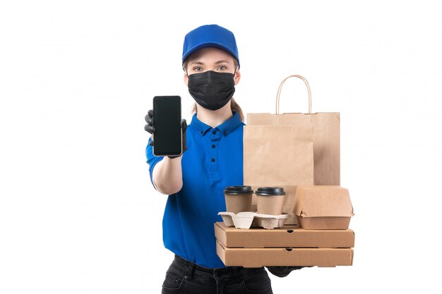 Un giovane corriere femminile di vista frontale in guanti neri uniformi blu e maschera nera che tiene i pacchetti di consegna dell'alimento