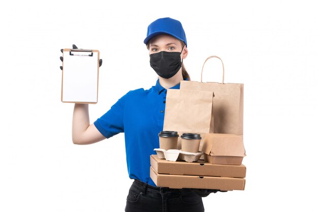 A front view young female courier in blue uniform black gloves and black mask holding food delivery packages