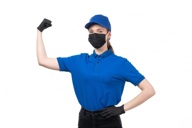 A front view young female courier in blue uniform black gloves and black mask posing and flexing