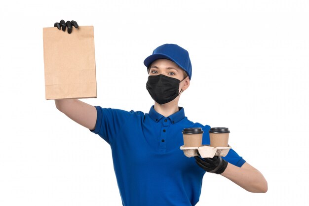 青い制服の黒いマスクとコーヒーカップとパッケージを保持している手袋の正面の若い女性宅配便