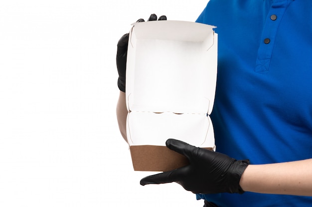 Молодая женщина-курьер в синей форме, черной маске и перчатках, держащая пустой пакет для доставки еды, вид спереди