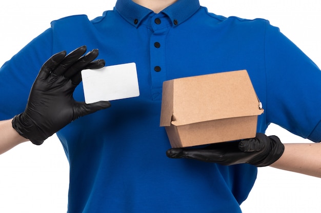 A front view young female courier in blue uniform black mask and gloves holding food delivery package