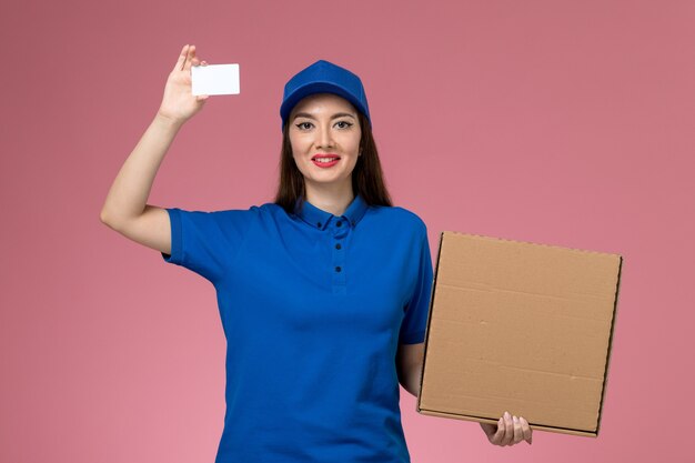 ピンクの壁に笑みを浮かべてフードボックスとカードを保持している青い制服と岬の正面図若い女性の宅配便