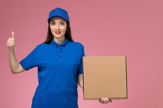 파란색 유니폼과 케이프 분홍색 벽에 음식 배달 상자를 들고 전면보기 젊은 여성 택배