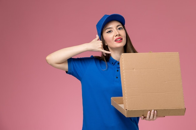 ピンクの壁にポーズをとって青い制服とケープ保持食品配達ボックスの正面図若い女性の宅配