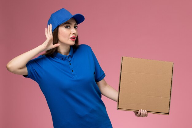 분홍색 벽에 들으려고 음식 배달 상자를 들고 파란색 유니폼과 케이프 전면보기 젊은 여성 택배