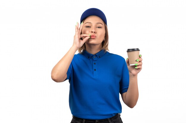 A front view young female courier in blue uniform holding coffee cup