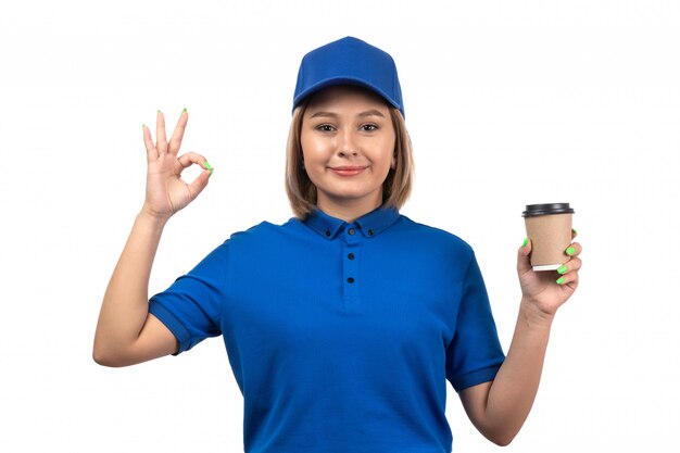 A front view young female courier in blue uniform holding coffee cup