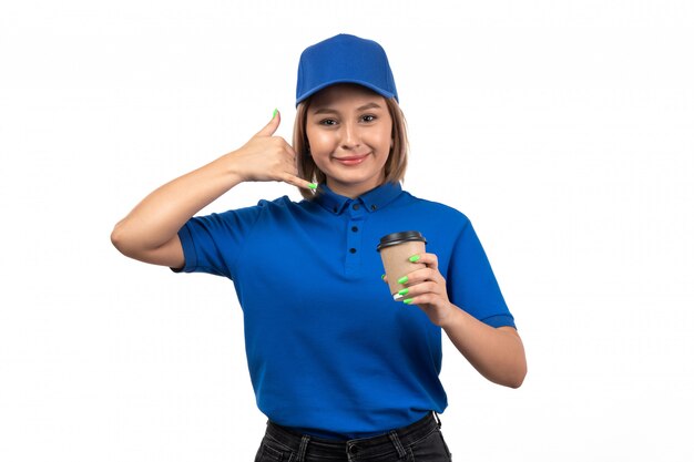 A front view young female courier in blue uniform holding coffee cup