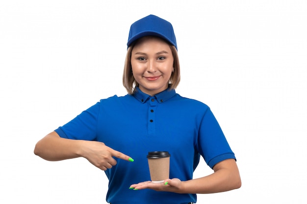 A front view young female courier in blue uniform holding coffee cup