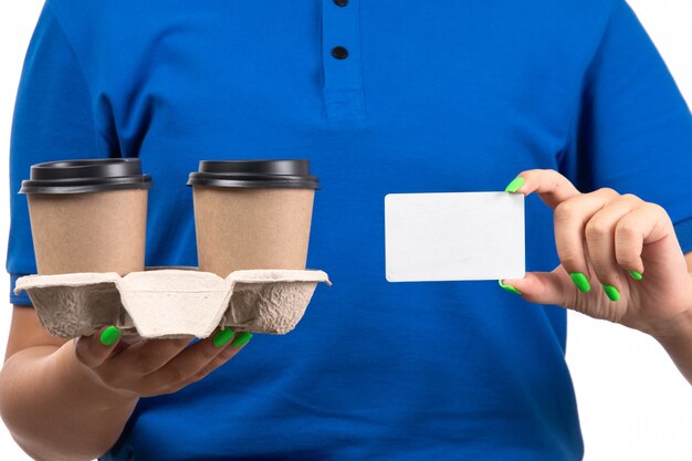 커피 컵과 흰색 카드를 들고 파란색 제복을 입은 전면보기 젊은 여성 택배
